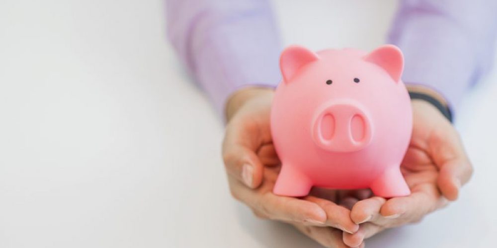 Businessman in a suit holding pink piggy bank with both hands, isolated on white background.