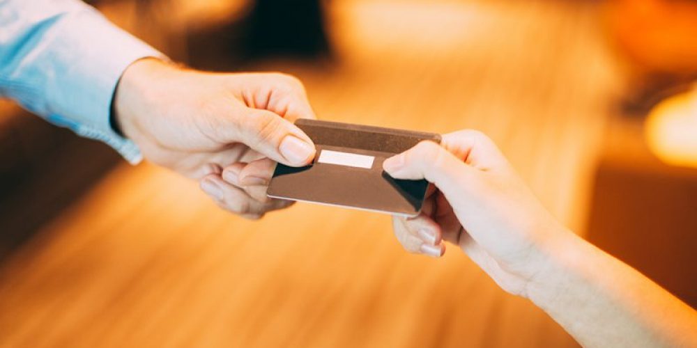 Male hand giving credit or debit card to female cashier for payment at shop or cafe