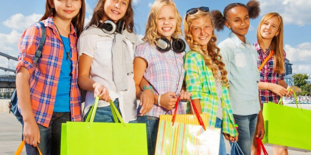 Friends with shopping bags walk together arm-in-arm in the city and smile happily in summer during daytime