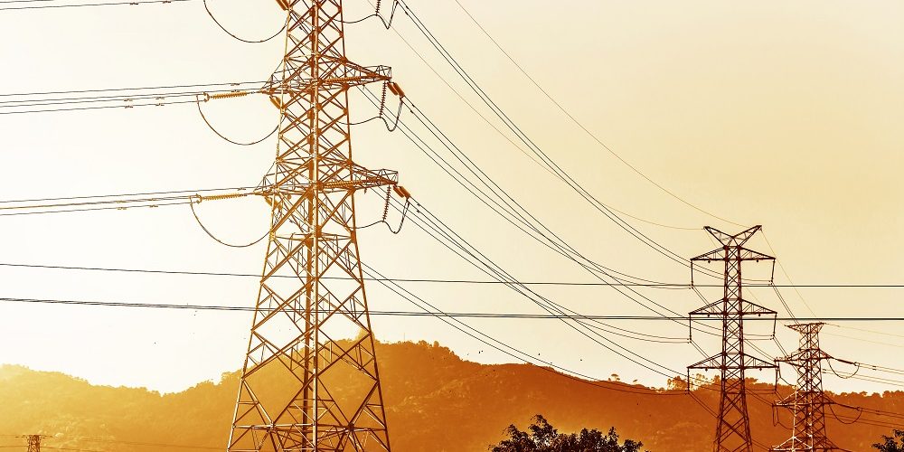 electricity transmission pylon silhouetted against blue sky at dusk